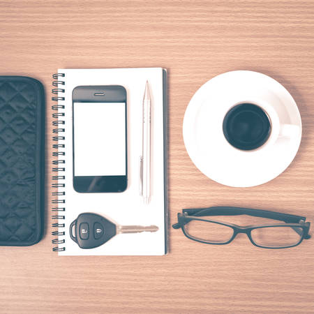 coffee and phone with notepad,car key,eyeglasses and wallet on wood table background vintage styleの写真素材