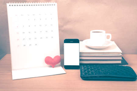 office desk : coffee with phone,wallet,calendar,heart,stack of book on wood background vintage styleの写真素材