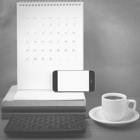 working table : coffee with phone,stack of book and wallet on wood background black and white colorの写真素材