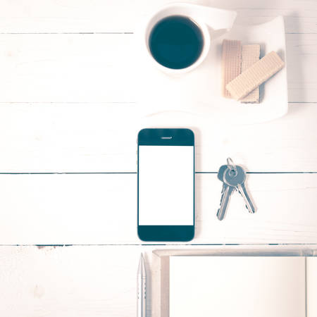 coffee cup with wafer,phone,key,notebook on white wood background vintage styleの写真素材