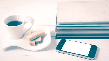 coffee cup with wafer,phone,stack of book on white wood background vintage styleの写真素材