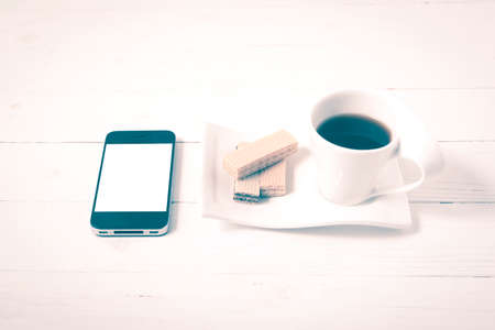 coffee cup with wafer and phone on white wood background vintage styleの写真素材