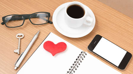 office desk : coffee and phone with key,eyeglasses,notepad,heart on wood backgroundの写真素材