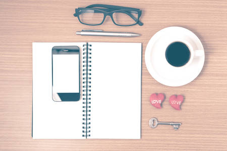 office desk : coffee and phone with key,eyeglasses,notepad,heart on wood background vintage styleの写真素材
