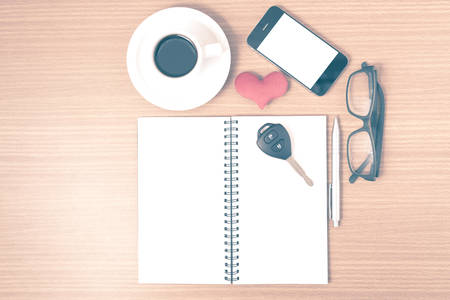 office desk : coffee and phone with car key,eyeglasses,notepad,heart on wood background vintage styleの写真素材