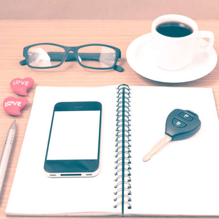office desk : coffee and phone with car key,eyeglasses,notepad,heart on wood background vintage styleの写真素材