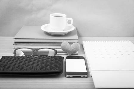 office desk : coffee with phone,stack of book,eyeglasses,wallet,calendar,heart on wood background  black and white colorの写真素材