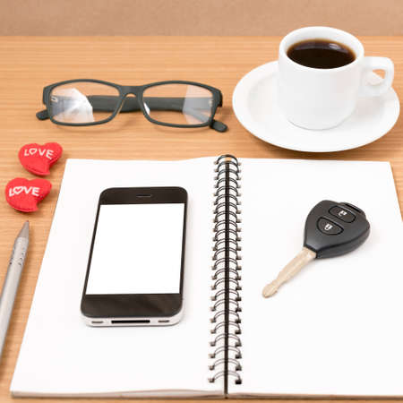 office desk : coffee and phone with car key,eyeglasses,notepad,heart on wood backgroundの写真素材