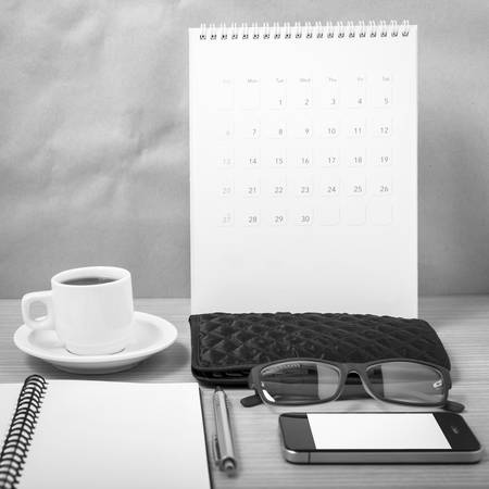office desk : coffee with phone, calendar, wallet, notepad on wood background black and white color toneの写真素材