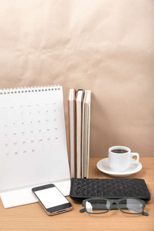 office desk : coffee with phone, stack of book, eyeglasses, wallet, calendar on wood backgroundの写真素材