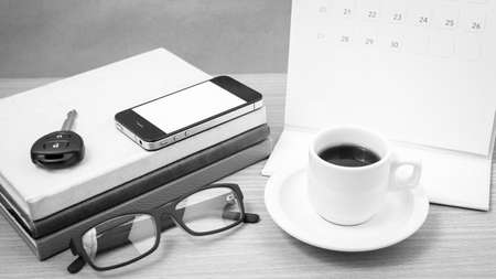 coffee and phone with car key, eyeglasses, stack of book, calendar on wood background black and...