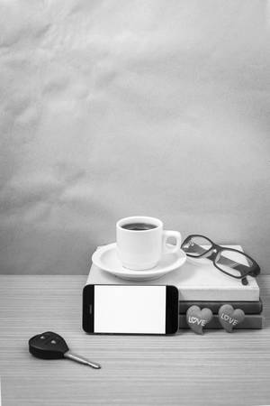 office desk : coffee and phone with car key, eyeglasses, stack of book, heart on wood background black and white toneの写真素材