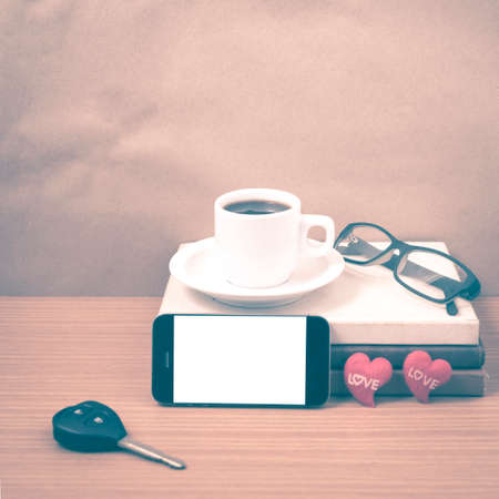 office desk : coffee and phone with car key, eyeglasses, stack of book, heart on wood background vintage styleの写真素材