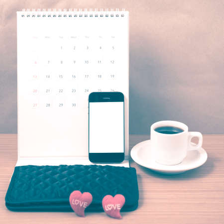 office desk : coffee with phone, calendar, wallet, heart on wood background vintage styleの写真素材
