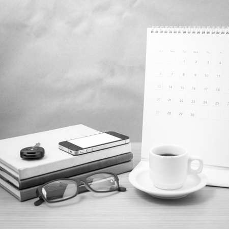 coffee and phone with car key, eyeglasses, stack of book, calendar on wood background black and white toneの写真素材