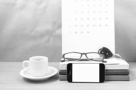 coffee and phone with car key, eyeglasses, stack of book, calendar on wood background black and white toneの写真素材