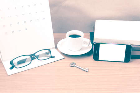 coffee and phone with key, eyeglasses, stack of book, calendar on wood background vintage styleの写真素材