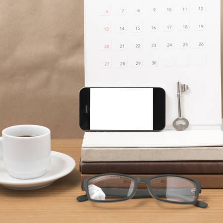 coffee and phone with key, eyeglasses, stack of book, calendar on wood backgroundの写真素材