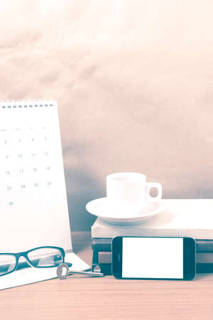 coffee and phone with key, eyeglasses, stack of book, calendar on wood background vintage styleの写真素材