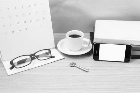 coffee and phone with key, eyeglasses, stack of book, calendar on wood background black and white...