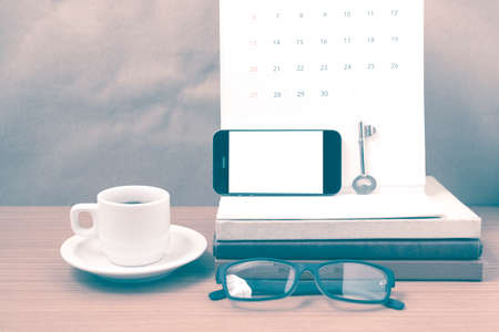 coffee and phone with key, eyeglasses, stack of book, calendar on wood background vintage styleの写真素材