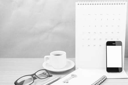 coffee and phone with key, eyeglasses, notepad, calendar on wood table background black and white toneの写真素材