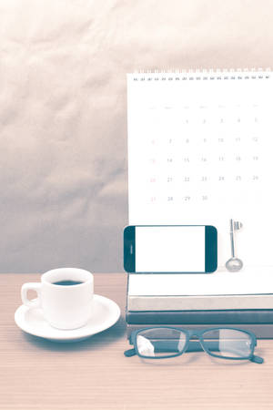 coffee and phone with key,eyeglasses,stack of book,calendar on wood background vintage styleの写真素材