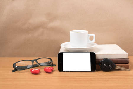 office desk : coffee and phone with car key,eyeglasses,stack of book,heart on wood background