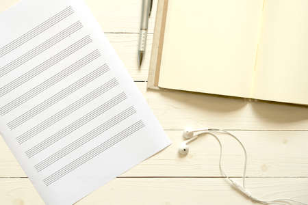 top view of music staff paper notebook and earphone on white wood backgroundの写真素材