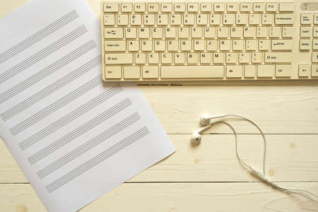 top view of computer keyboard earphone and music staff paper on white wood backgroundの写真素材
