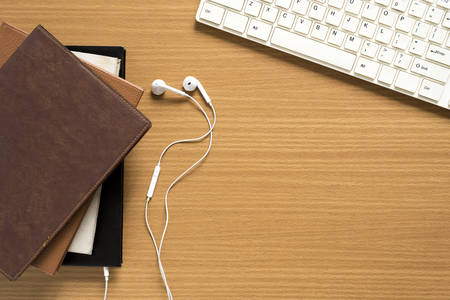 top view of stack of notebook with earphone and computer keyboard on wood backgroundの写真素材