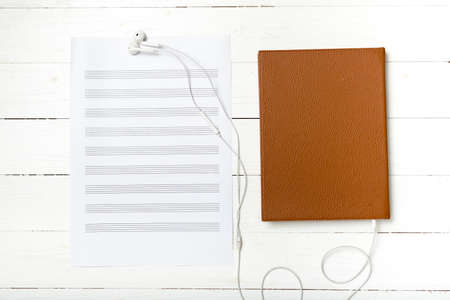 top view of earphone music staff paper and book on white wood backgroundの写真素材