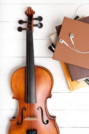 top view of violin with stack of book and earphone on white wood backgroundの写真素材