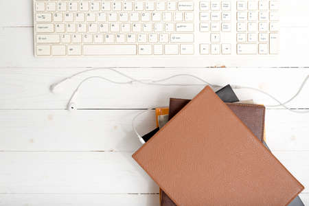 top view of earphone with computer keyboard with stack of book on white wood backgroundの写真素材