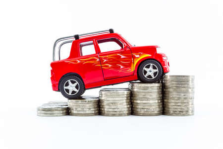 Red car over a lot of stacked coins isolated on white background.の写真素材