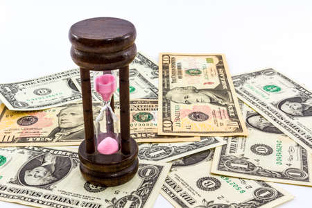 Closeup of hourglass on a heap of paper dollars.