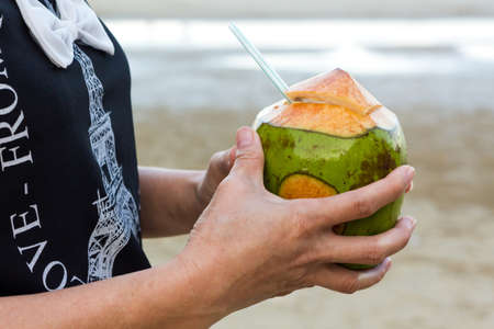 Woman hand holding coconut on tropical beach. の写真素材