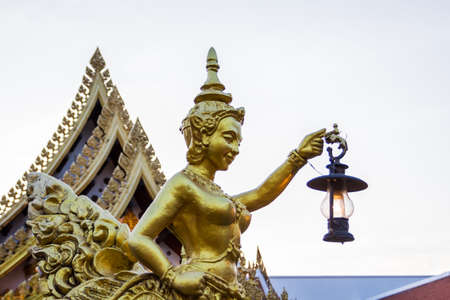 Goldent Ginnaree statue art holding a lamp,Thai temple,Thailand.の写真素材