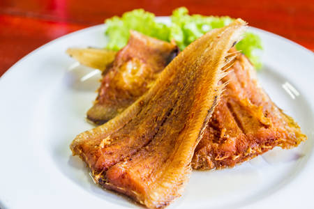 Fried fish with vegetables on white dish.