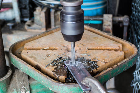 Industrial technician working on a drilling machine, making a hole in a metal.