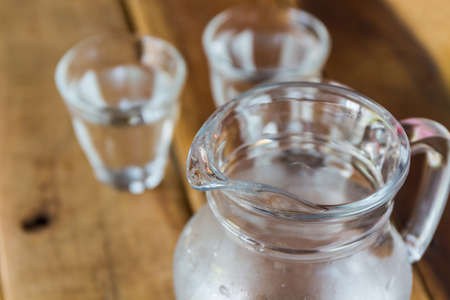 Glass pitcher of water and glass on wood background.