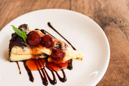 Chocolate brownie cheesecake with cherry fruit on white plate.