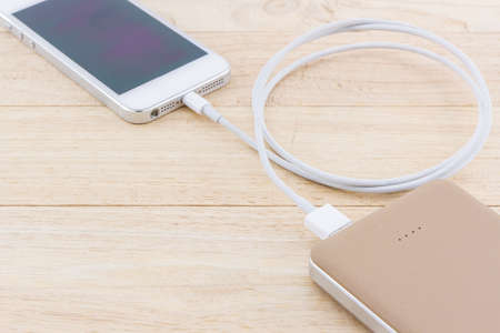 Smartphone with golden power bank on wood desk.