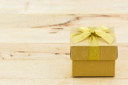 Golden gift box with ribbon bow on wooden table.の写真素材