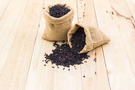 Rice berry in small burlap sack on wood background.の写真素材