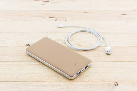 Golden powerbank and USB cable for smartphone on wood background.の写真素材