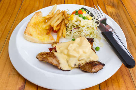 Grill pork steak under white sauce, French Fries (potato chips) and vegetable salad on a white plate.の写真素材