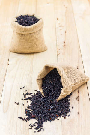 Rice berry in small burlap sack on wood background.の写真素材