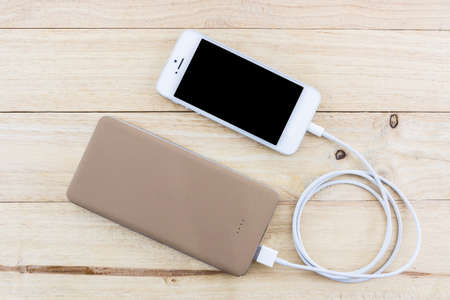 Smartphone with golden powerbank on wood desk.