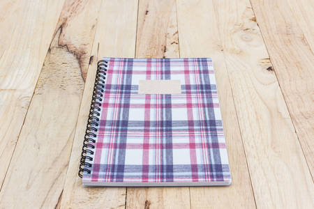Fabric plaid texture cover spiral notebook on wood background.